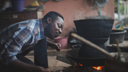Native African man blowing the fire  cook in the kitchen with happy.16:9 style
