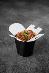 Wok in box spicy noodles in black food container. Fast food delivery service. Takeaway chinese street meal.