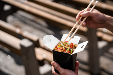 Wok in box in black food container. Holding spicy noodles with chopsticks. Fast food delivery service. Takeaway chinese street meal.