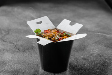 Wok in box rice noodles in black food container. Fast food delivery service. Takeaway chinese...