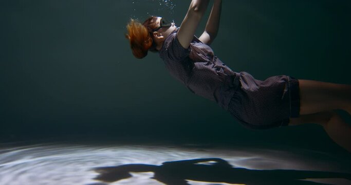 Cinematic side view of young beautiful woman in pyjamas, eye mask sink under water, falling asleep dreaming slow motion.