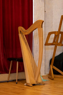 Rehearsal setup with large wooden harp in front of a red theatre curtain with stool and music sheet stand. Musical instrument in theatrical setting.