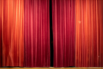 Theatrical curtain with shades of bright vibrant red with a small opening hanging over a wooden...