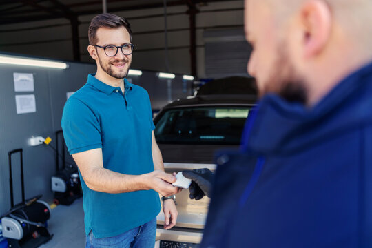 Handing over the keys at the technical inspection. The client leaves the car key to the car service worker Close up of a man with glasses in casual clothes hands over the key to the master in the shop