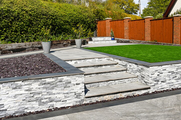 Steps from a patio to path and artificial grass in a residential back garden landscaped with light...