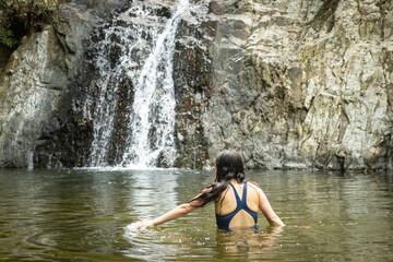 Mujer con el agua hasta la cintura caminando por un rio en medio de la naturaleza junto a una cascada