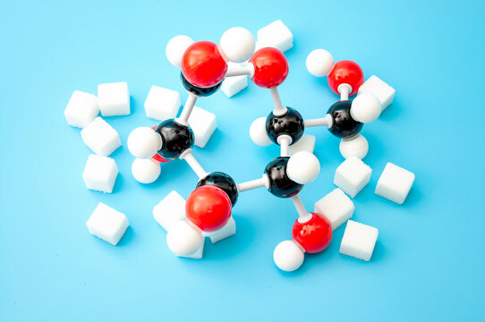 Simple sugars, diabetes awareness and chemical structure of carbohydrates concept with plastic model of the glucose molecule and sugar cubes isolated on blue background
