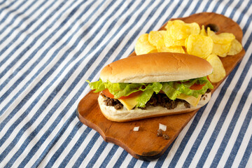 Homemade Chopped Beef Sandwich with Potato Chips on a rustic wooden board, side view. Copy space.