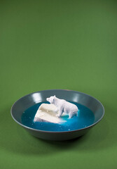 Tiny kid toy polar bear floating on cheese on a plate in blue water. Environment protection, endangered species, natural habitat and global warming concept.