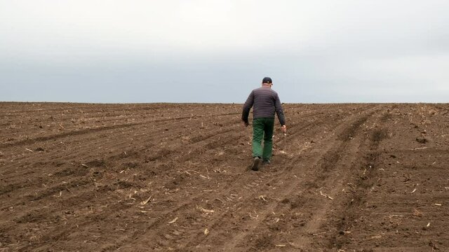 Man agronomist walks through a plowed field. View from the back.