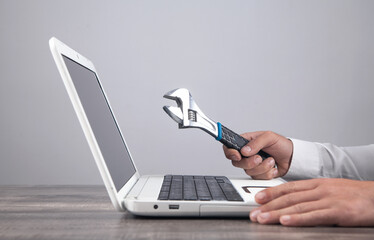 Male hand showing adjustable wrench over computer keyboard. IT Service. Support