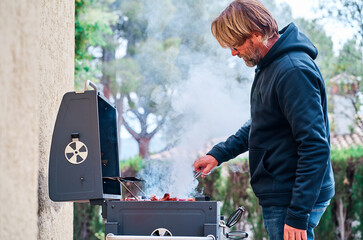 Middle-aged man cooking meat on barbecue grill