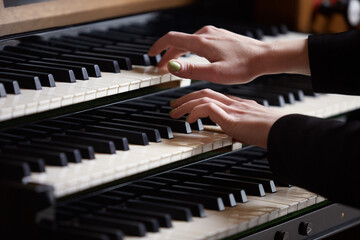Fototapeta premium Close- up of a woman's hands playing a three-manual electronic organ. Musical education concept.