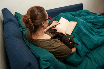 a woman reading a book with a cat in her arms