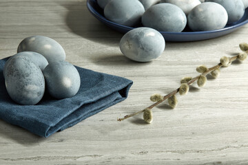 Colored blue-gray marble eggs lie on a cloth and in a plate on a gray textured background