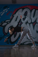 Fototapeta na wymiar Silhouette of young woman hiphop dancer (breakdancer)dancing on graffiti studio background. Contrast colors.