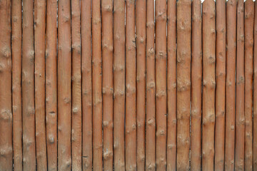 Log pine fence. Round wooden fence from shot vertical pine logs. A fence made of roughly processed boards. A palisade of rough logs. Wood background