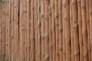 Log pine fence. Round wooden fence from shot vertical pine logs. A fence made of roughly processed boards. A palisade of rough logs. Wood background