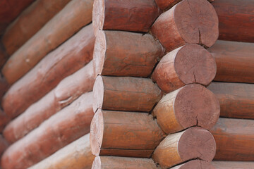 Frame log wooden house. A fragment of the wall of the house, built of round wooden logs and painted brown. The house is made of natural wood and is environmentally friendly.