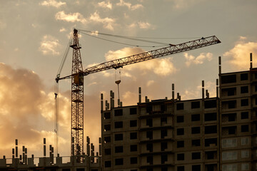 The silhouette of a building under construction. Sunset silhouettes of high-rise buildings under construction with cranes against the sky with clouds and the setting sun