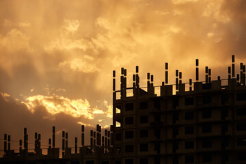 The silhouette of a building under construction. Sunset silhouettes of high-rise buildings under construction against the sky with clouds and the setting sun