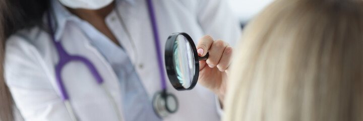 Dermatologist examines patient's face through magnifying glass