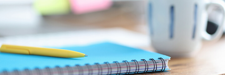 On table is cup next to pen and diary for notes