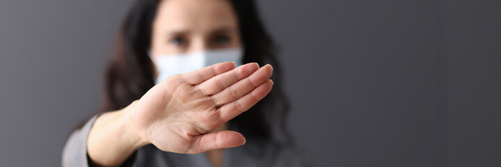 Woman in medical protective mask holds her hands in negative gesture
