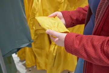 Caucasian pregnant woman chooses yellow windbreaker from the rain in store to buy. The concept of fashion and wardrobe updates. Hands close up