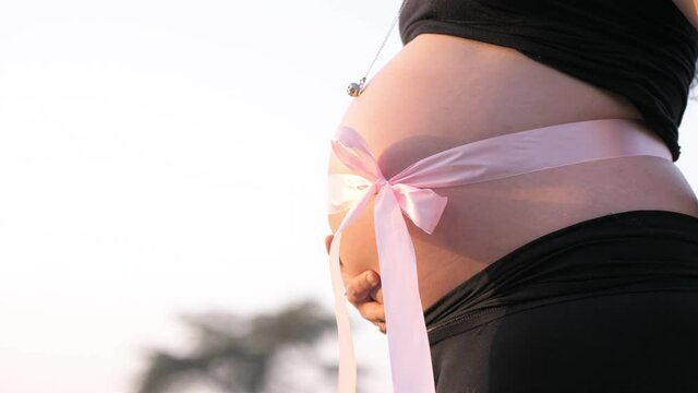 belly of pregnant woman with a pink bow that heralds the birth of a baby girl
