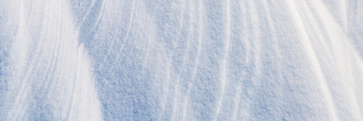 Beautiful winter background with snowy ground. Natural snow texture. Wind sculpted patterns on snow surface. Wide panoramic texture for background and design.