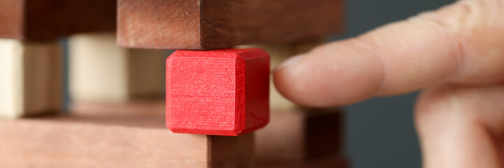 Wooden tower made of wooden brown cubes from which red cube is taken