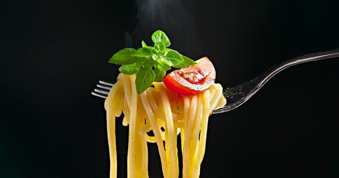 Fork with spaghetti, tomato and basil isolated on a black background. Hot spaghetti with steam