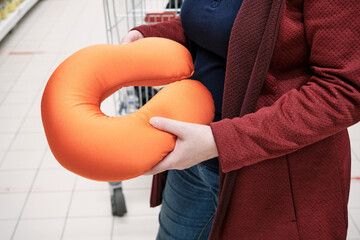 Pregnant caucasian woman wearing a mask against the virus buys a pillow in a store to support her...