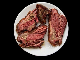 Cut slices of roasted beef brisket on a white plate over black background