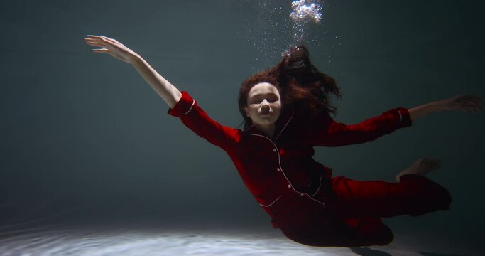 Amazing cinematic portrait of young beautiful woman in red pyjamas slowly sinking under water falling asleep slow motion