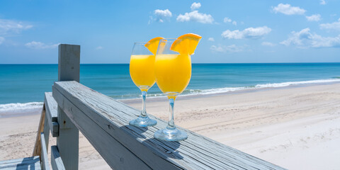 Two glasses brightly lit by the sun with a mimosa cocktail against the background of the blue sea...