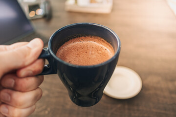 Blue mug of hot chocolate on dark wooden table in a cafe.