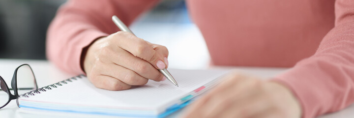 Woman holds pen in her hands and makes notes in diary