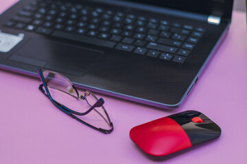 Laptop glasses and mouse on pink background