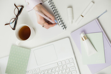 Female hands writes in notebook on Office white desktop. Planning Remote working from home. Freelancers laptop, cup, spectacles. Concept of distance learning, isolation, female business