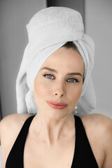 Beauty portrait of a cheerful attractive woman with a towel on her head and looking at camera, lying on bed.