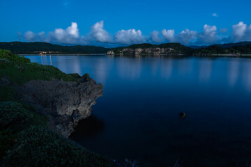 Peaceful long exposure after sunset. Serene sea with its smooth surface, mountains in the background, traces of star and rock from the cliff being illuminated by the soft remaining light of the sunset