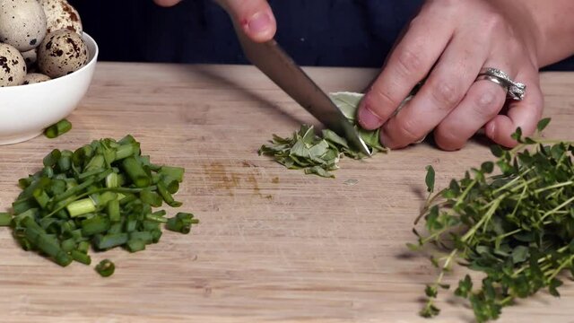Close up of knife chopping or dicing fresh basil on wooden cutting board for restaurant or home food preparation