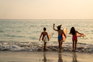 Confidence Asian woman girl friends in swimwear holding surfboard and walking together on the beach at summer sunset. Female friendship enjoy outdoor activity lifestyle play extreme sports surfing