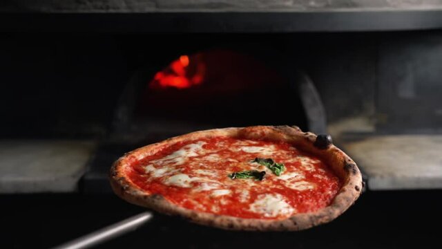 Close-up slow motion shot of a chef taking out a traditional Italian margherita pizza from a wood oven. Neapolitan Restaurant and Pizzeria in Italy. Mozzarella, basilico and tomato sauce.