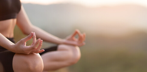 Close up with selective focus of hands woman sitting in yoga lotus pose outdoor at sunrise, meditating for balance. Horizontal banner view for website header design with copy space for text.  - obrazy, fototapety, plakaty