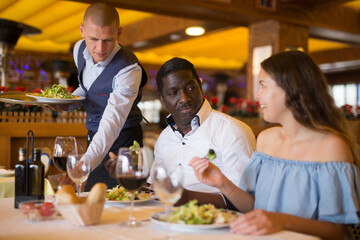 Elegant waiter serving company at restaurant, bringing food for man and woman guests