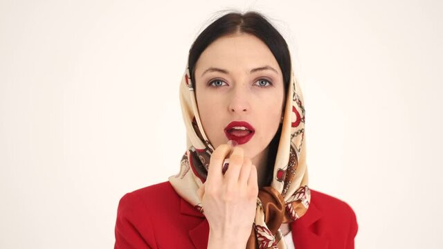 Woman in shawl apply res lipstick in white studio