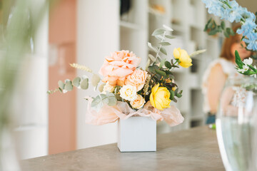 Flower arrangement with yellow and pink roses and eucalyptus in gift box on table in the flower shop, modern floristic